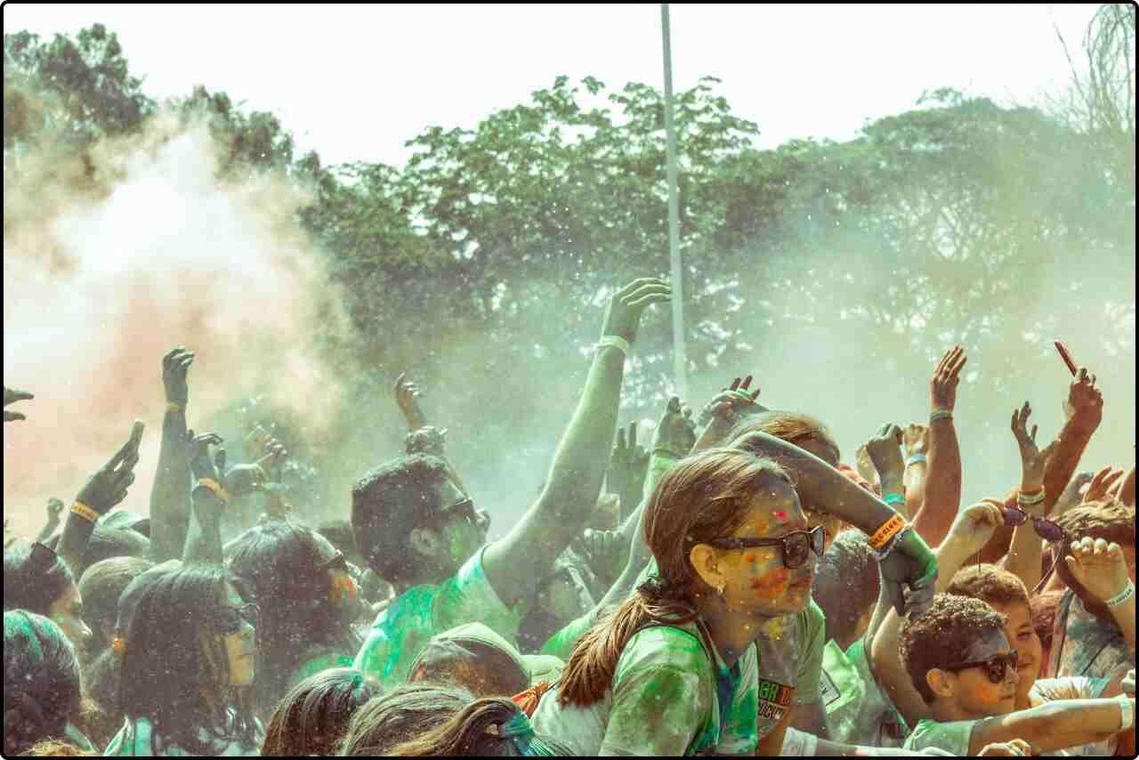 Crowd of people enjoying various activities at a lively festival with colorful powder.